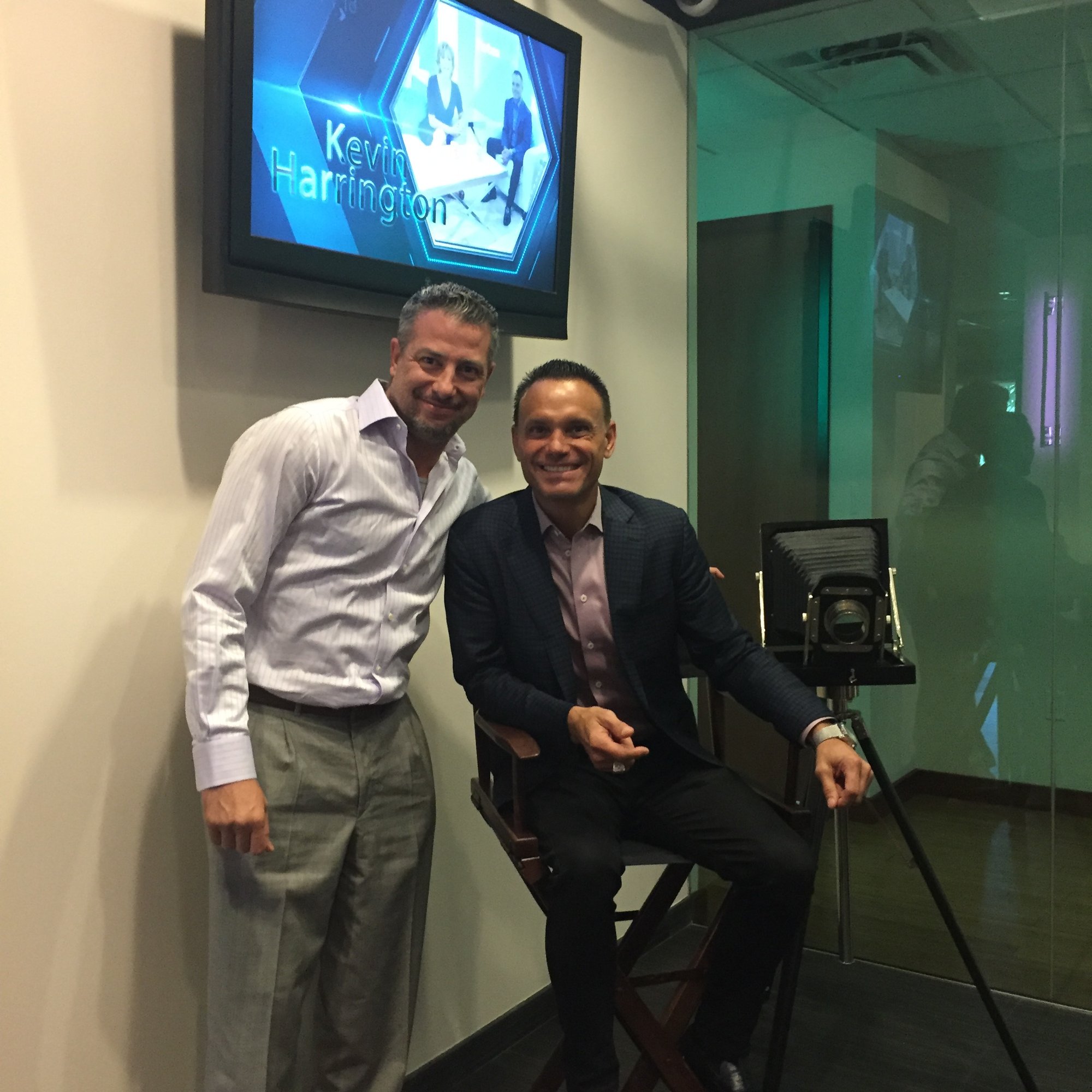Spotlight Media founder with Kevin Harrington seated beside a vintage studio camera