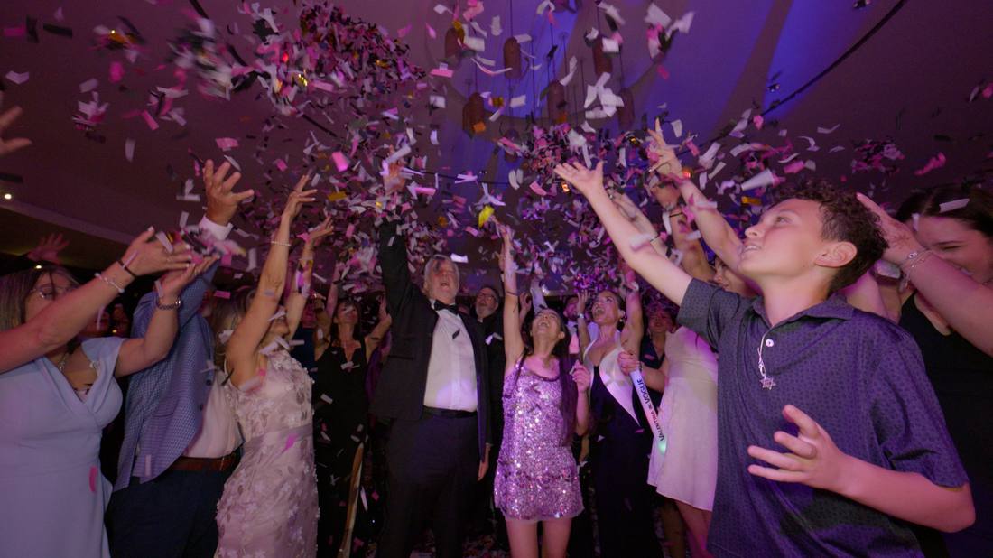 Guests reaching up as pink and white confetti rains down over the celebration