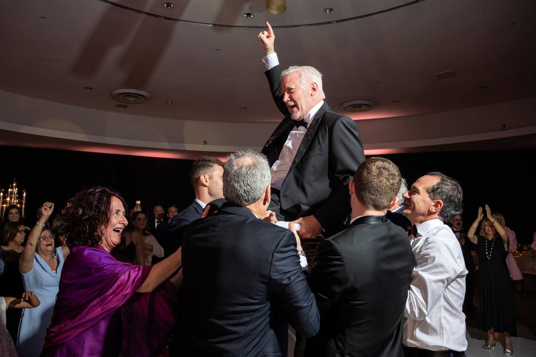 Guest lifted overhead by well-wishers, pointing toward the ceiling in celebration
