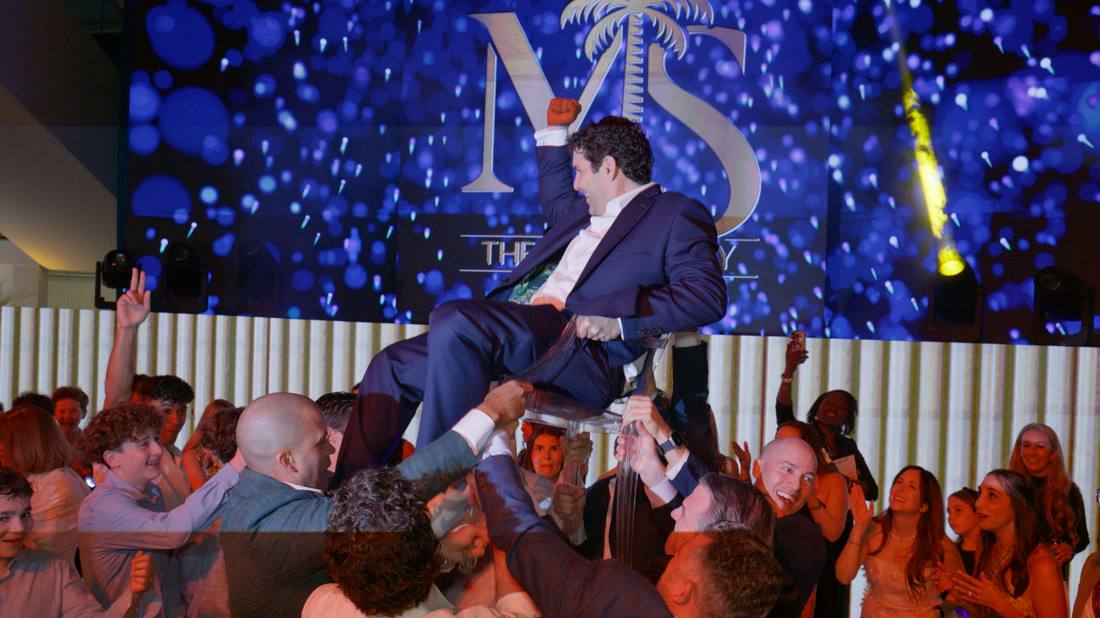 Guest lifted overhead cheering in front of an illuminated event sign