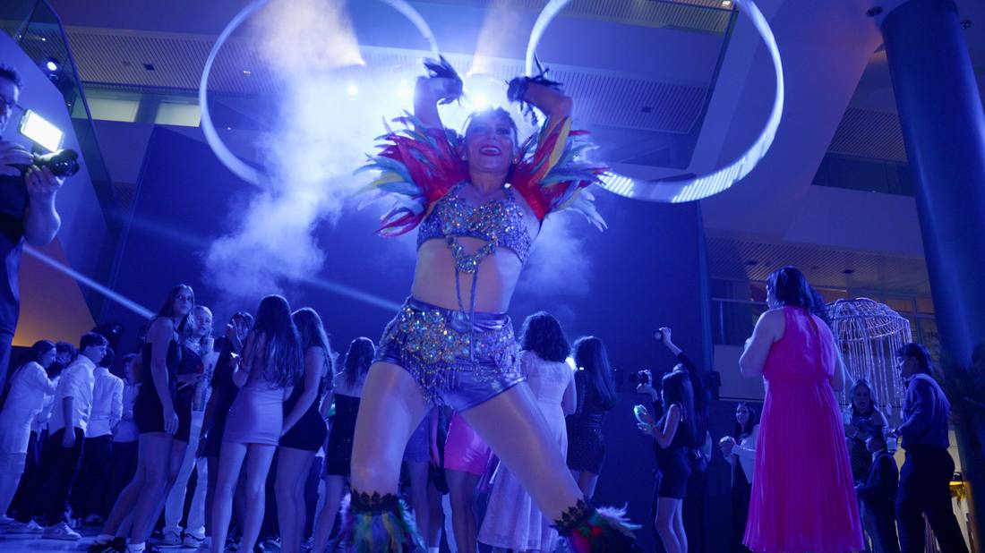 Performer in a feathered costume dancing beneath illuminated LED hoops