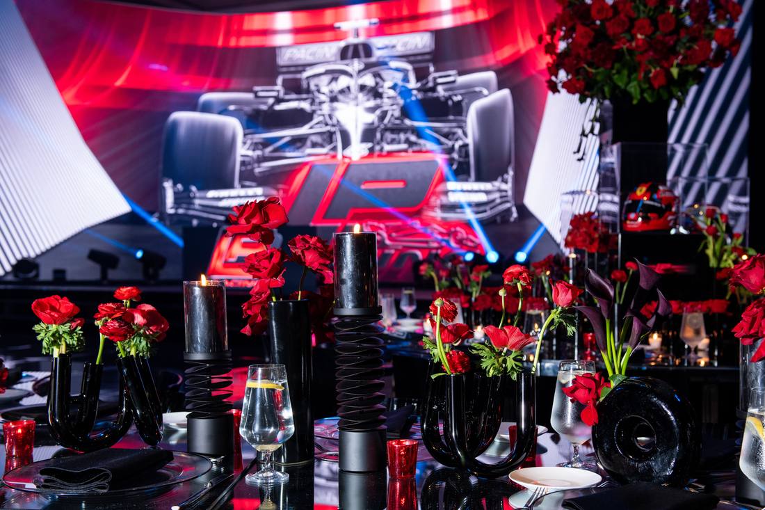 Motorsport-themed reception table with red florals and a race car video backdrop