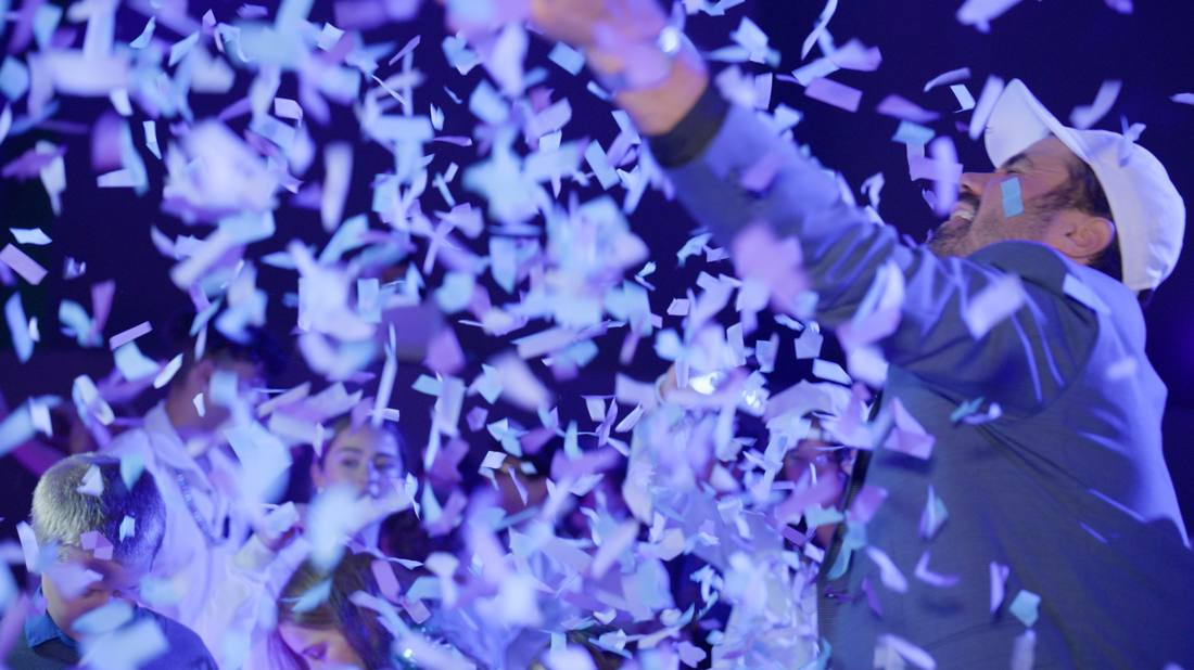 Guest in a white hat reaching up through falling confetti
